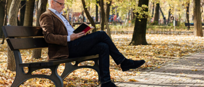 An elderly gentleman reading a book on a park bench